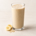 Banana oats protein shake in a clear glass with banana and oats.